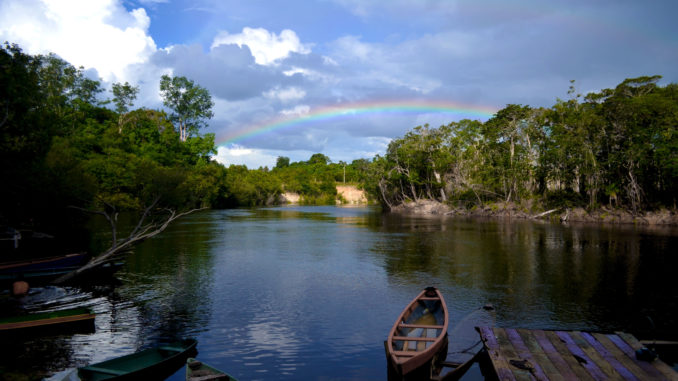 Foto de arco íris e canoas na margem de rio na cidade de Borba (AM)