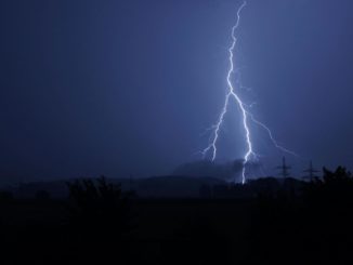 Foto de raio atingindo torre de transmissão de energia em um campo aberto.